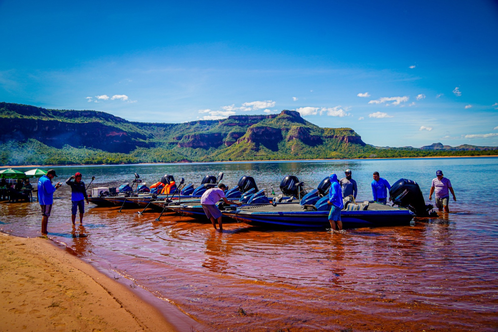 Frota de bass boats ancorados na praia com montanhas ao fundo