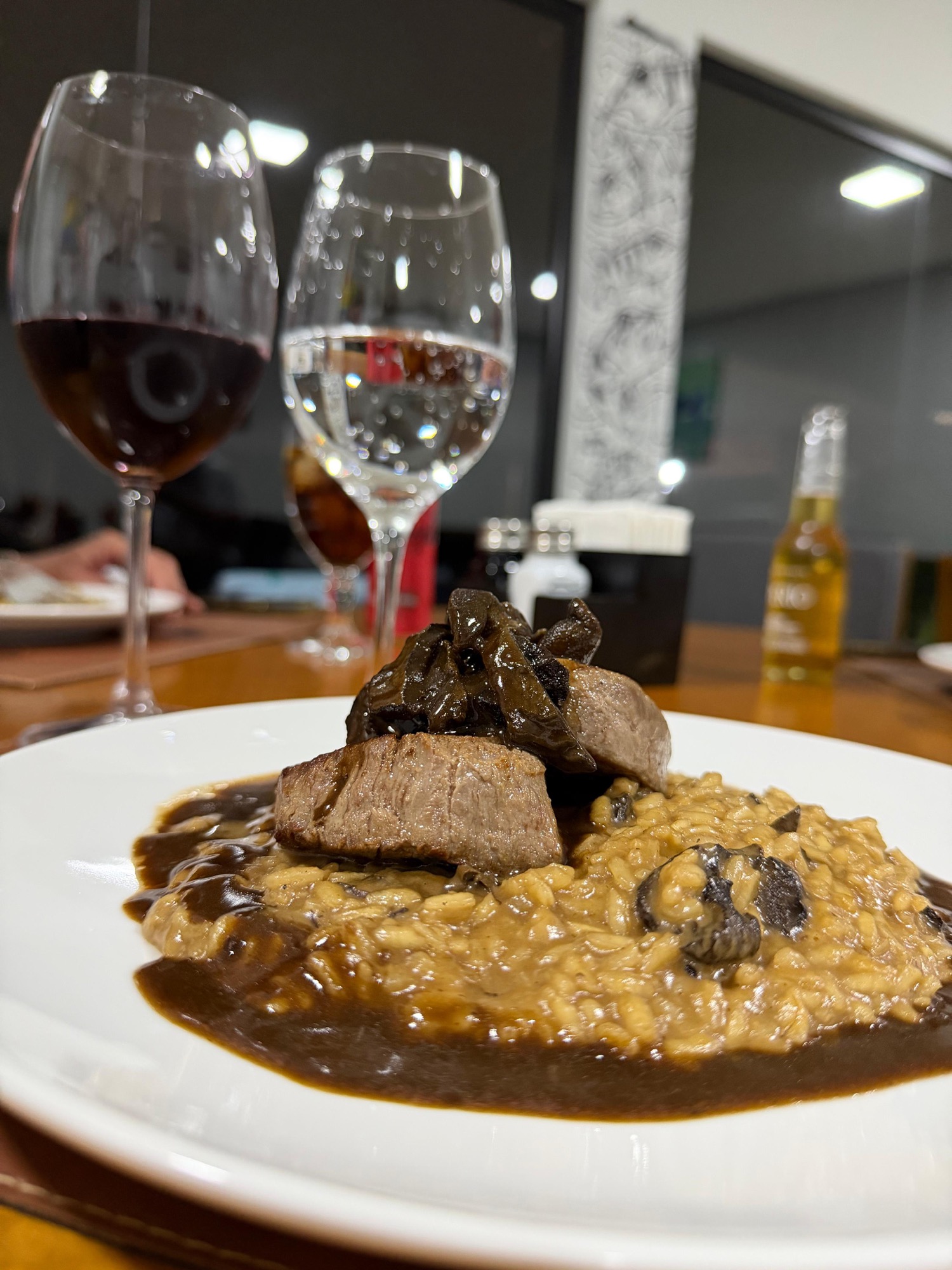 Prato gourmet de risoto com filé e cogumelos acompanhado de taças de vinho no restaurante do Manso Fishing Resort