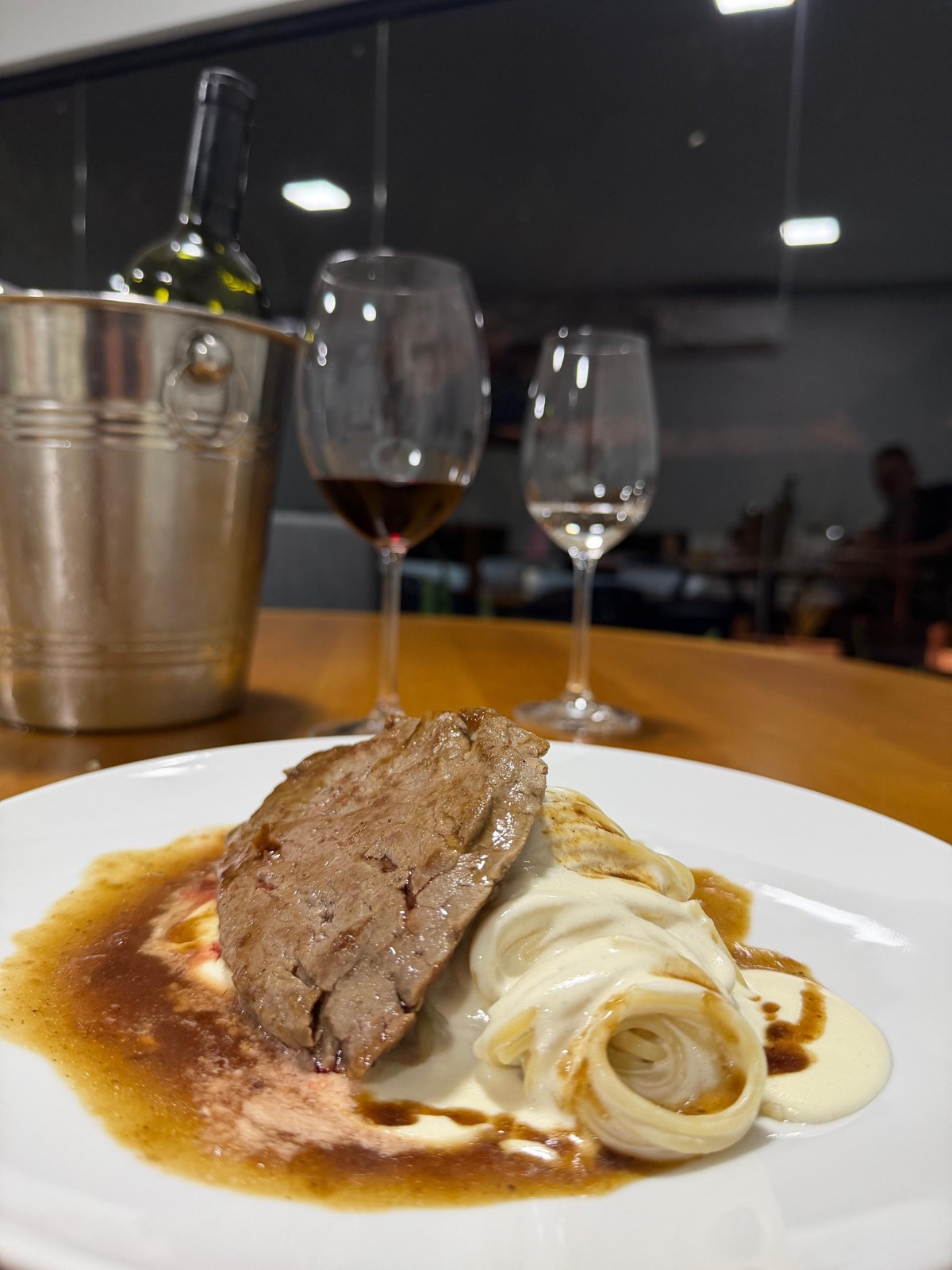 Prato refinado com carne e molho acompanhado de taças de vinho